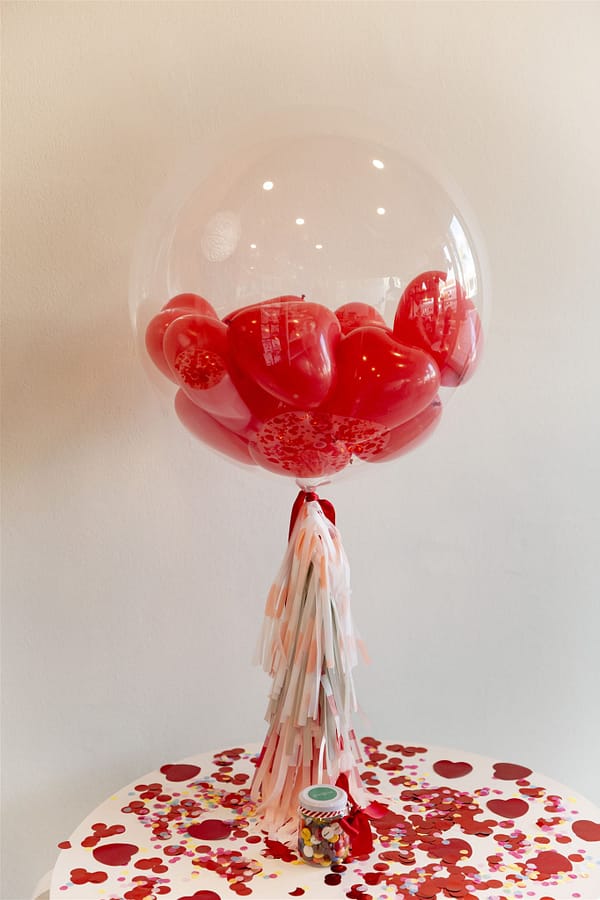 Globo transparente de 60cm. relleno de globos pequeños de coraozones e inflado con helio