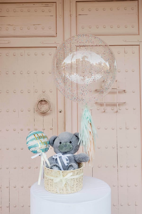 Peluche de oso de color gris en cesta grande con globo celeste de Baby boy y globo transparente inflado con helio